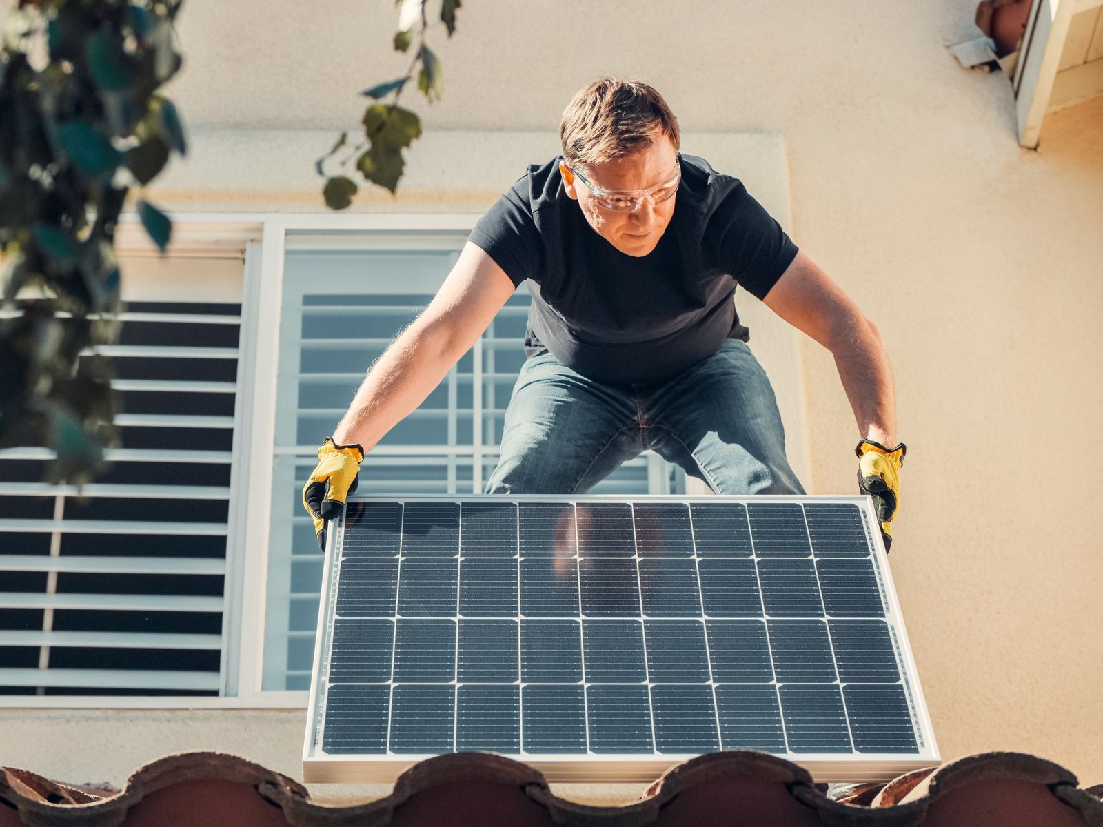 Monteur trägt ein Photovoltaikmodul auf ein Ziegeldach